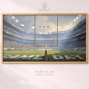 May include: A framed artwork depicting a football stadium on game day. The painting shows a green field with the words "GAME DAY" and a goalpost. American flags wave in the background. The artwork is framed in a light wood.