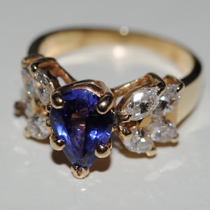 May include: A gold ring with a pear-shaped sapphire gemstone surrounded by smaller diamonds.