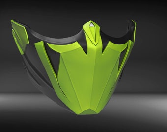 Può includere: Una maschera facciale nera e verde con un design geometrico. La maschera ha una forma affilata e angolare ed è realizzata in un materiale liscio e duro.