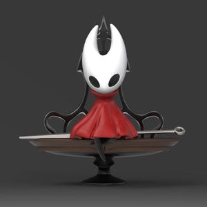 May include: A 3D-rendered figurine of a character from the video game Hollow Knight. The character has a white head with black eyes, a red cape, and is seated on a decorative platform with a spear. The platform is supported by a black stand.