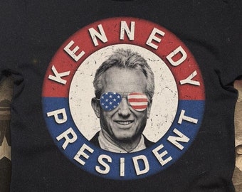 Könnte beinhalten: Schwarzes T-Shirt mit einem kreisförmigen Grafikdruck im Vintage-Stil, der einen Mann mit Sonnenbrille und dem Text "KENNEDY PRESIDENT" zeigt.