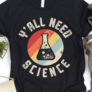 May include: A black t-shirt featuring a vintage-style graphic of a beaker and the text "Y'all Need Science".