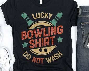 May include: Black t-shirt with a vintage-style graphic of bowling pins and a ball. The text on the shirt reads "Lucky Bowling Shirt* Do Not Wash".
