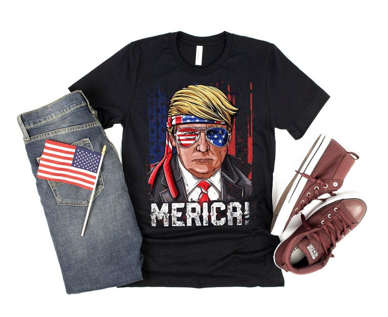 Peut inclure: T-shirt noir avec une image de dessin anim&eacute; d'une personne portant un bandana rouge, blanc et bleu et des lunettes de soleil. Le texte "MERICA!" est imprim&eacute; sous l'image.