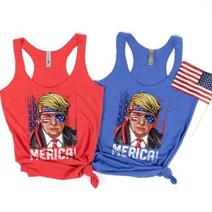 Peut inclure: Deux d&eacute;bardeurs avec un motif repr&eacute;sentant une personne portant un bandana rouge, blanc et bleu et des lunettes de soleil. Le texte "Merica!" est imprim&eacute; sur chaque d&eacute;bardeur. Un d&eacute;bardeur est rouge et l'autre est bleu.