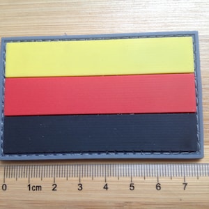 May include: A black, red and yellow fabric patch with a stitched border. The patch is approximately 6 cm wide and 4 cm tall.