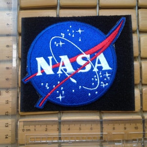 May include: Embroidered NASA patch featuring the iconic blue circle with the white NASA text and red swoosh. The patch is on a black square background. The patch measures approximately 3.5 inches wide.