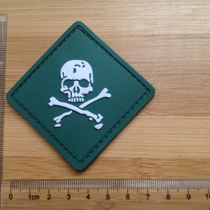 May include: A green diamond-shaped patch with a white skull and crossbones design. The patch is approximately 5 cm wide.