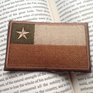 May include: A brown, tan, and green embroidered patch of the Texas state flag. The flag features a white star on a green background, a tan stripe, and a brown stripe.