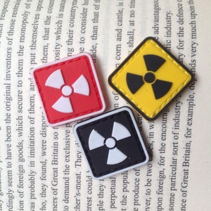 Peut inclure: Trois patchs de couleurs différentes avec un symbole de radiation. Les patchs sont carrés, en forme de diamant et ronds. Les patchs sont rouge, jaune et noir.