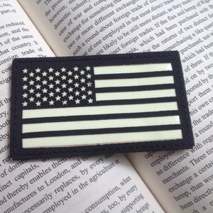 Könnte beinhalten: Ein schwarz-weißes amerikanisches Flaggen-Patch mit einem Leucht-im-Dunkeln-Design. Das Patch ist aus strapazierfähigem Material gefertigt und hat einen Klettverschluss.