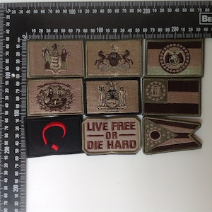 Op de afbeelding: Een verzameling van negen geborduurde patches met verschillende ontwerpen. De patches zijn beige, bruin en groen met rode en witte accenten. De patches bevatten het staatszegel van Pennsylvania, een rode halve maan en de tekst "Live Free or Die Hard".