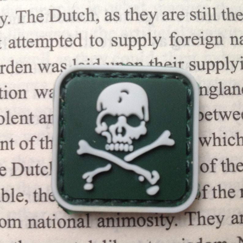 May include: A green fabric patch with a white skull and crossbones design. The patch is square and has a stitched border.