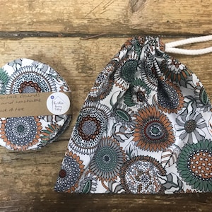 May include: A set of reusable cotton face rounds and a matching drawstring bag. The rounds are stacked and labeled "cotton face rounds, reusable and washable, pack of five." The bag and rounds feature a floral pattern in white, orange, green, and blue.