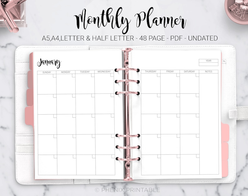 May include: A white monthly planner with a pink binder. The planner is open to January and has a grid layout with spaces for each day of the week. The text "Monthly Planner" is written in black cursive at the top of the page. The text "A5,A4,LETTER & HALF LETTER - 48 PAGE - PDF - UNDATED" is written in black below the title. The text "January" is written in black cursive at the top of the left page. The text "YEAR" is written in black at the top of the right page.