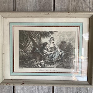 Peut inclure: Impression vintage encadrée représentant une scène pastorale en noir et blanc avec deux personnages en costume d'époque. L'impression est encadrée dans un cadre en bois clair vieilli avec une bordure turquoise et marron. Le texte "LES DÉLICES DE L'AUTOMNE" est visible.