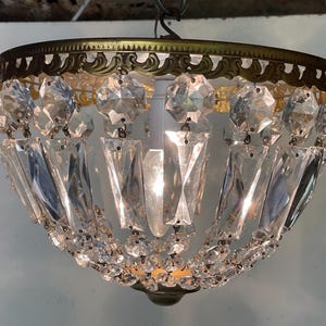 Peut inclure: Un lustre en cristal vintage avec une monture en métal de couleur laiton. Le lustre présente de multiples pendentifs et accents en cristal clair et facetté, créant une apparence étincelante et élégante. Le luminaire est conçu pour être monté au plafond.