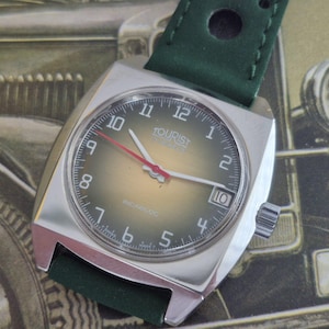 Peut inclure: Une montre-bracelet vintage avec un boîtier carré argenté et un bracelet en cuir vert. Le cadran de la montre est vert foncé avec des chiffres et des aiguilles blancs, et une trotteuse rouge. La montre indique "TOURIST" et "INCABLOC".