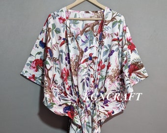 May include: White cotton kaftan with a floral print featuring birds and flowers. The kaftan has a tie at the waist and 3/4 sleeves.