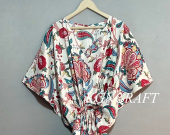 May include: A white, floral-patterned kaftan dress with red, blue, and green accents. The dress features a tie waist and wide sleeves, hanging on a wooden hanger. The word "CRAFT" is visible on the dress.