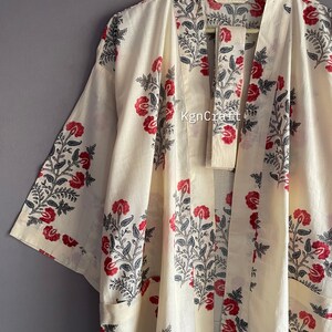Pu&ograve; includere: Un kimono in cotone bianco con una stampa floreale in tonalit&agrave; di rosso e nero. Il kimono ha una cintura da legare e una silhouette lunga e fluida.