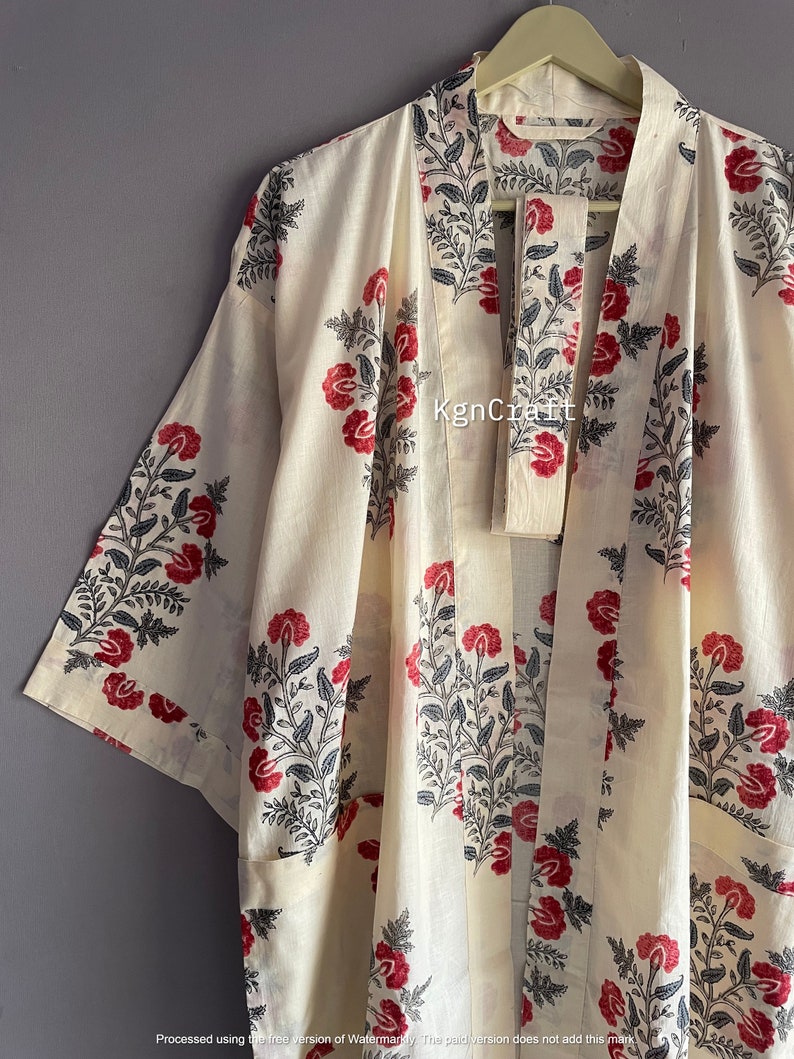Pu&ograve; includere: Un kimono in cotone bianco con una stampa floreale in tonalit&agrave; di rosso e nero. Il kimono ha una cintura da legare e una silhouette lunga e fluida.