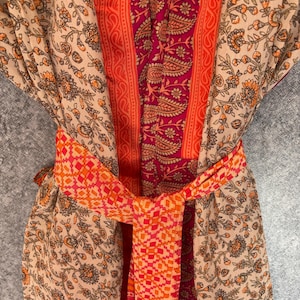 May include: A patterned robe with a tied belt. The robe features a beige floral print with orange accents, a central panel of paisley and orange stripes, and a geometric patterned belt in shades of orange and red.