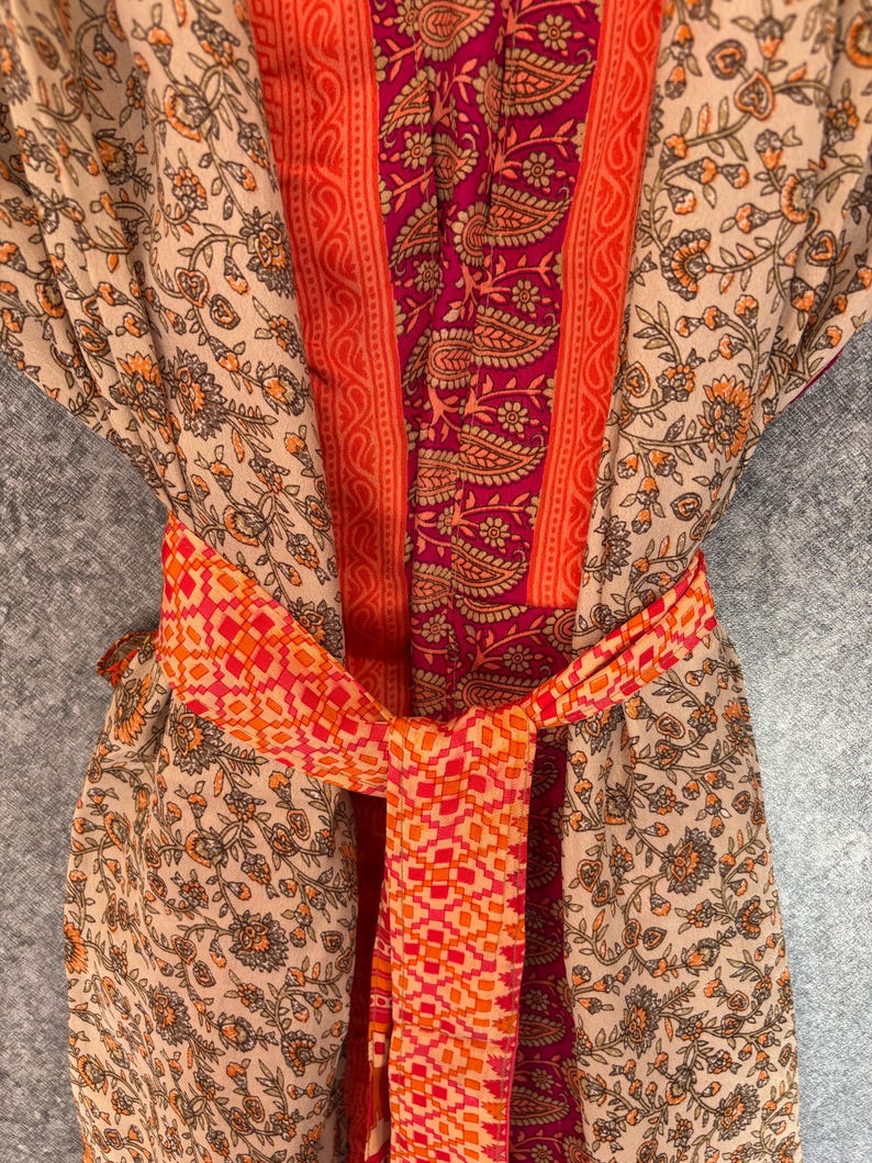 May include: A patterned robe with a tied belt. The robe features a beige floral print with orange accents, a central panel of paisley and orange stripes, and a geometric patterned belt in shades of orange and red.