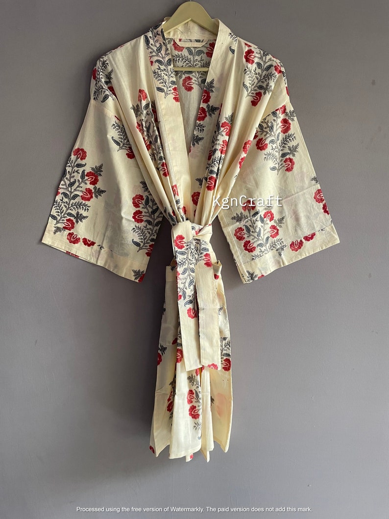 Pu&ograve; includere: Una vestaglia in cotone color crema con stampa floreale in tonalit&agrave; di rosso, grigio e nero. La vestaglia ha una cintura da legare e maniche lunghe.