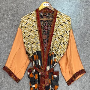 May include: A colorful kimono robe with a patterned design. The robe features a mix of colors, including orange, black, yellow, and red. The sleeves are a solid orange color, and the robe is tied with a matching belt.
