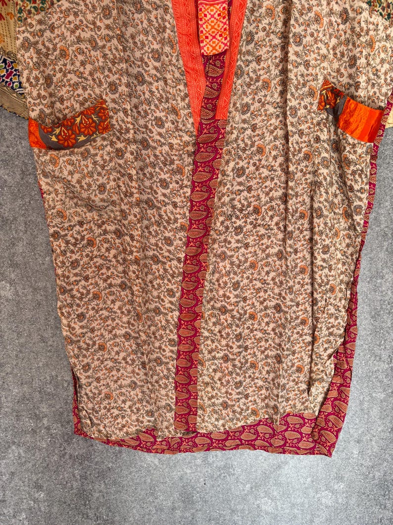 May include: A beige kimono-style robe with a floral pattern. The robe features orange trim along the edges and pockets, and a paisley border. The fabric appears soft and lightweight, suitable for layering or lounging.
