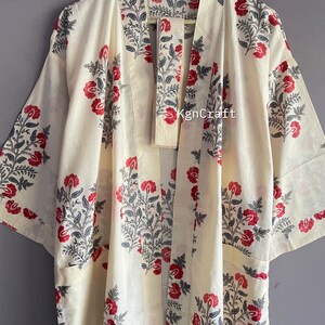 Pu&ograve; includere: Un kimono color crema con una stampa floreale in tonalit&agrave; di rosso, nero e grigio. Il kimono ha una chiusura a nodo e due tasche. Il testo "KgnCraft" &egrave; visibile sul davanti del capo.