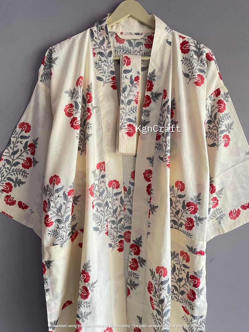 Pu&ograve; includere: Un kimono color crema con una stampa floreale in tonalit&agrave; di rosso, nero e grigio. Il kimono ha una chiusura a nodo e due tasche. Il testo "KgnCraft" &egrave; visibile sul davanti del capo.