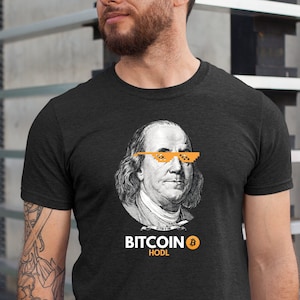 May include: A black t-shirt with a graphic of Benjamin Franklin wearing pixelated sunglasses and the text "BITCOIN HODL" with a Bitcoin symbol.