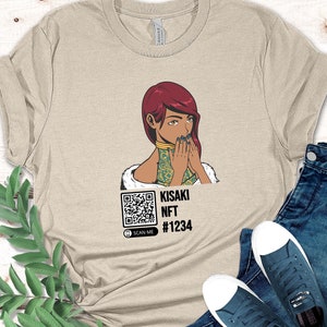May include: Beige t-shirt featuring a graphic of a woman with red hair and a QR code. The text "KISAKI NFT #1234" is below the graphic. The shirt is paired with blue jeans and navy sneakers.