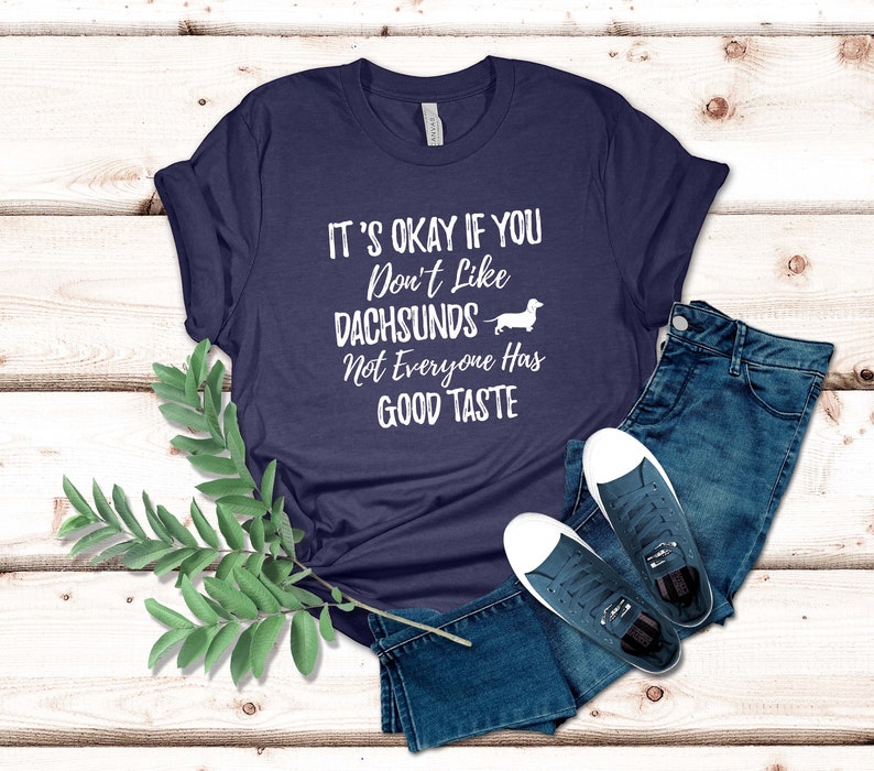 May include: A navy blue t-shirt with white text that reads "It's okay if you don't like dachshunds. Not everyone has good taste." A white dachshund silhouette is next to the text.