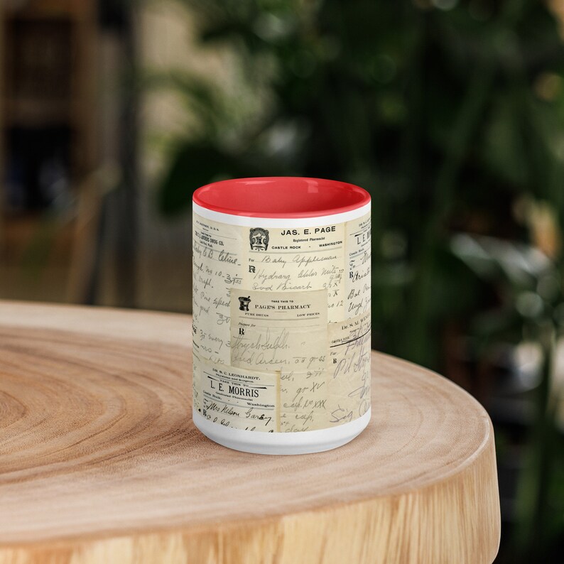 Op de afbeelding: Een witte keramische mok met een rode rand heeft een vintage ontwerp van handgeschreven recepten en apotheeklabels. De mok is bedrukt met de tekst "JAS. E. PAGE" en "PAGEN'S PHARMACY".