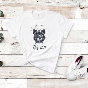 May include: White t-shirt with a black and white alarm clock graphic and the text "Wake Up! It's 11:11"