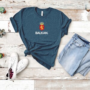 K&ouml;nnte beinhalten: Ein dunkelblaues T-Shirt mit einem wei&szlig;en Aufdruck eines Wappens und dem Wort "BALKAN."
