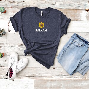 May include: A navy blue t-shirt with a white graphic of a coat of arms and the word "BALKAN."