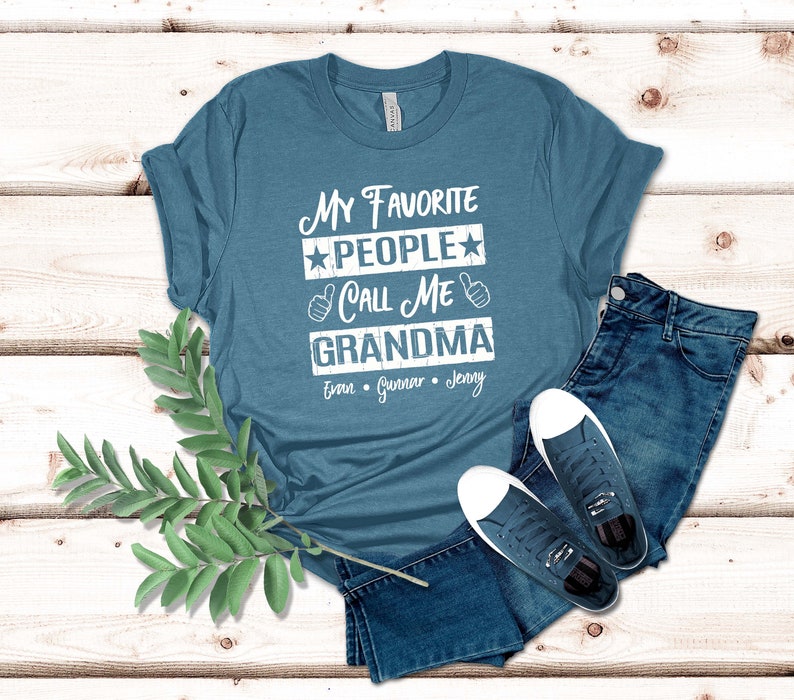 May include: A teal blue t-shirt with the text "My Favorite People Call Me Grandma" in white with stars and thumbs up. The names "Evan, Gunner, Jenny" are printed below the text.