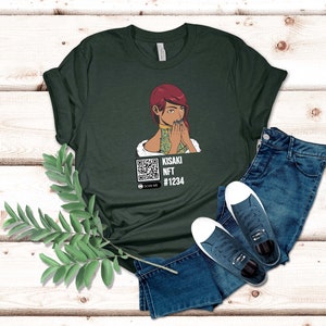 May include: Dark green t-shirt featuring an illustration of a woman with red hair and a QR code. The text on the shirt reads "KISAKI NFT #1234" with a "SCAN ME" prompt. The shirt is paired with blue jeans and white-soled sneakers.