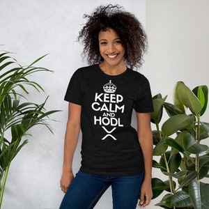 Puede incluir: Una camiseta negra con el texto blanco "KEEP CALM AND HODL", una corona y un s&iacute;mbolo. La persona lleva vaqueros azules. Se ven plantas verdes en el fondo.