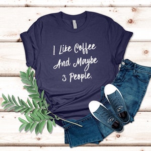 May include: A navy blue t-shirt with white text that reads "I like coffee and maybe 3 people."