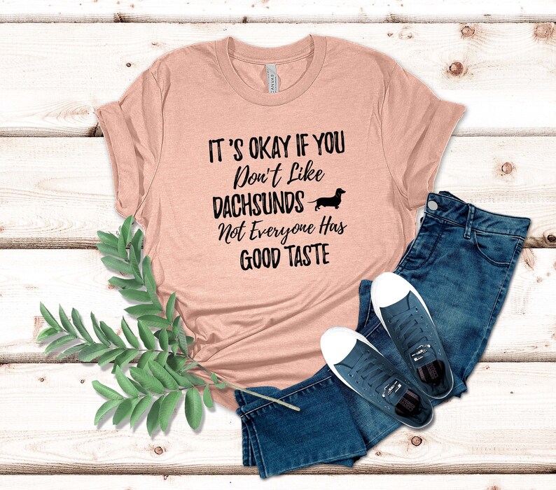May include: A peach-colored t-shirt with the text "It's okay if you don't like dachshunds. Not everyone has good taste." and a black silhouette of a dachshund.