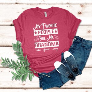 May include: Red t-shirt with the text "My Favorite People Call Me Grandma" and the names "Evan, Gunner, Jenny" printed on it.