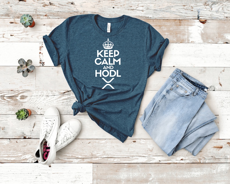Puede incluir: Una camiseta de color verde azulado con las palabras "KEEP CALM AND HODL" en blanco, un gr&aacute;fico de corona y un s&iacute;mbolo "X". Se combina con vaqueros azules de lavado claro y zapatillas blancas. Peque&ntilde;as suculentas en macetas est&aacute;n dispersas.