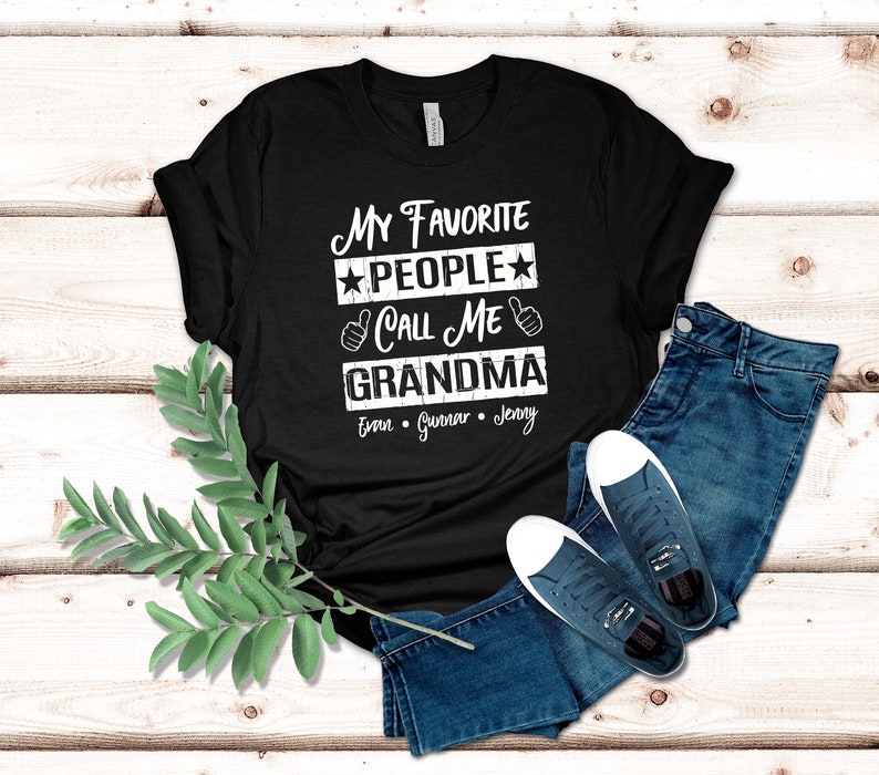 May include: Black t-shirt with white text that reads "My Favorite People Call Me Grandma" with the names Evan, Gunnar, and Jenny underneath.