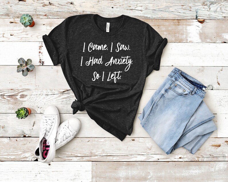 May include: A dark grey t-shirt with the text "I came. I saw. I had anxiety. So I left." printed in white.