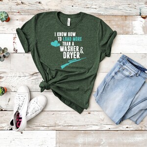 May include: A green t-shirt with the text "I know how to load more than a washer & dryer" and a rifle graphic. The shirt is laid out on a wooden surface with a pair of white sneakers and blue jeans.